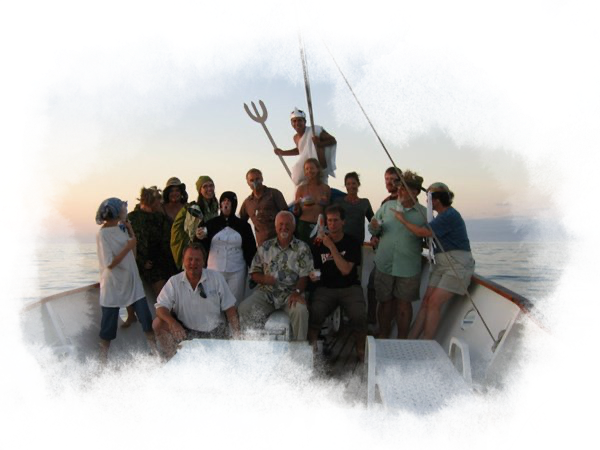 Group photo of travelers on a galapagos cruise enjoying a fun celebration on deck. One traveler is standing on the nose of the ship dressed as Poseidon.