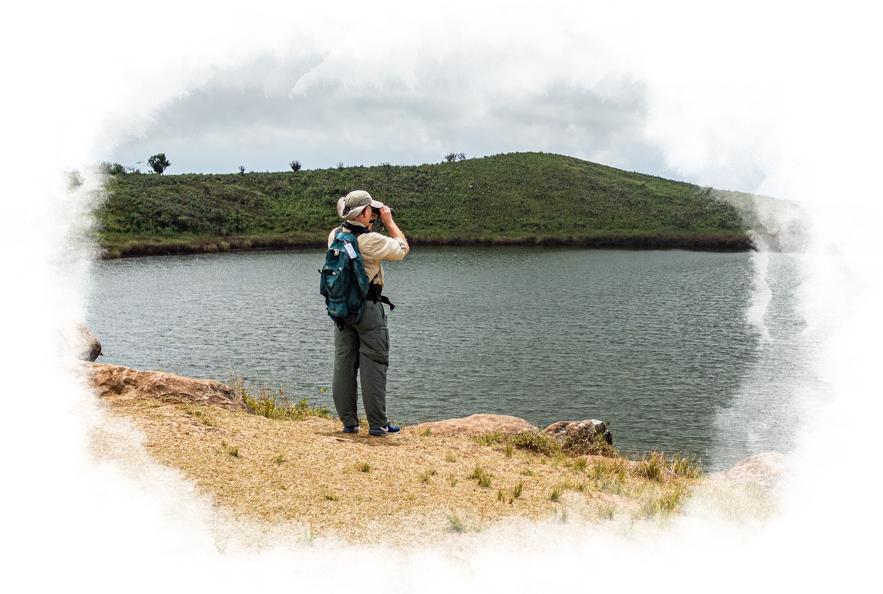A man standing on land, looks into his binoculars.