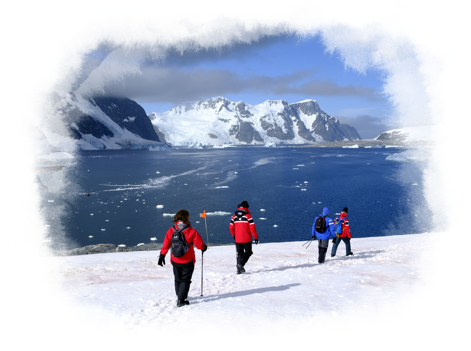 A few people walk across the snowy landscape near the water.