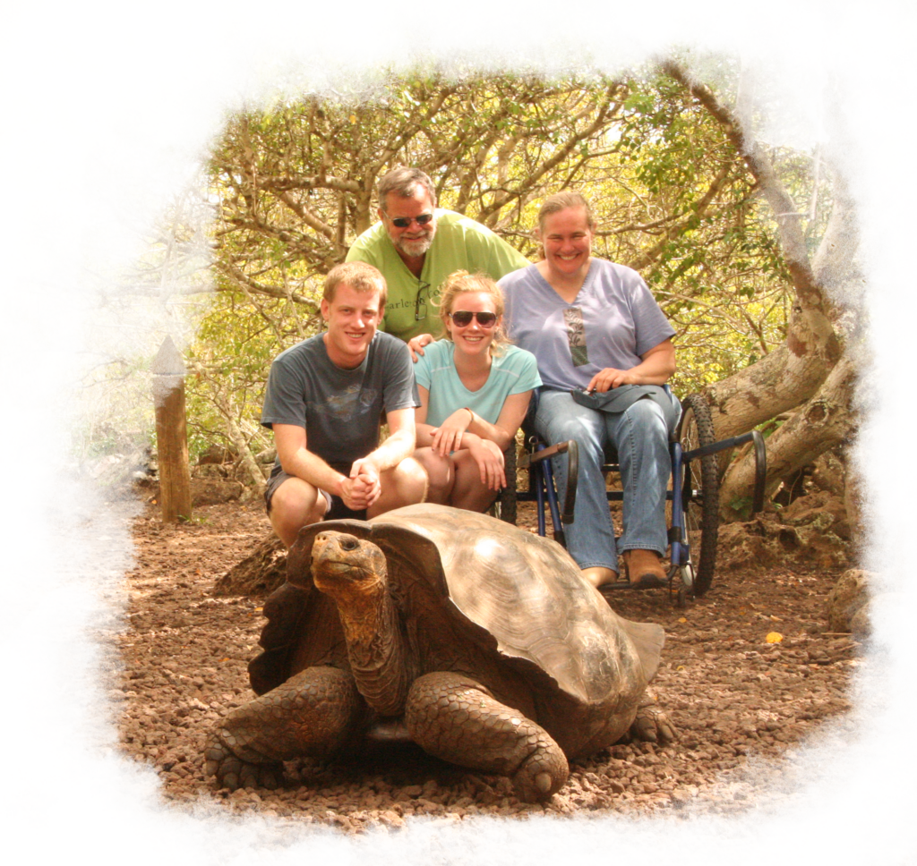 A family of four sits a few feet behind a tortoise, smiling. The mother is in a wheelchair, comfortably enjoying the tour and time with her love-ones.
