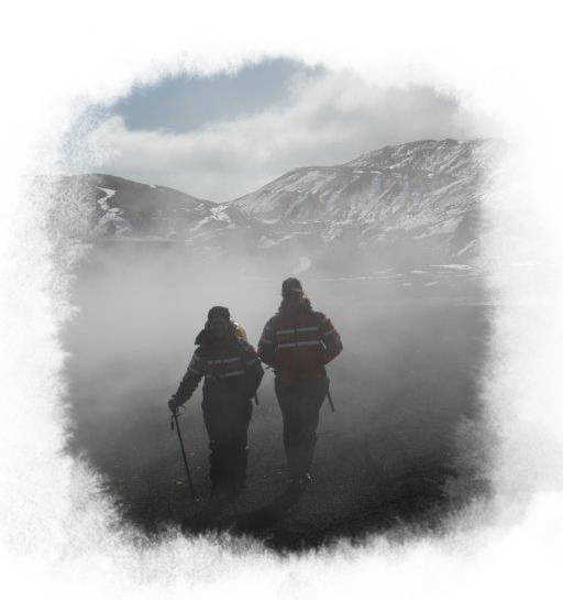 Two travelers wearing hiking gear, smiling. Mountains fill the background.